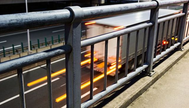 Metal railing framing blurred truck streaks on urban highway at night, bolts visible