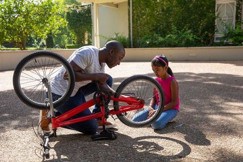 Father teaching daughter bike repair in sunny driveway