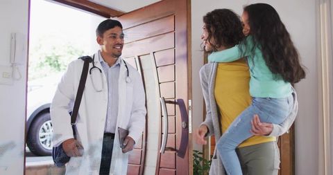 Hispanic Doctor Greeting Mother Holding Child During Home Visit for Family Healthcare