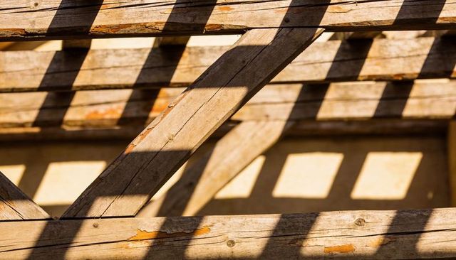 Sunlit weathered pergola casting geometric shadows on stucco wall with peeling paint