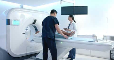 Technologist positioning patient for ct scan on advanced scanner in bright radiology suite