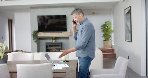 Senior Man Multitasking with Phone and Paperwork at Home