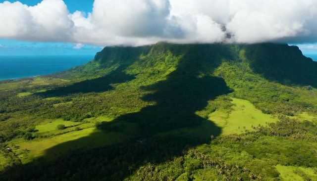 Cloud-capped mesa casting giant shadow over lush tropical valley and coastal rainforest