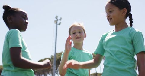 Diverse children giving high five on sunny sports field, teamwork and joyful youth energy