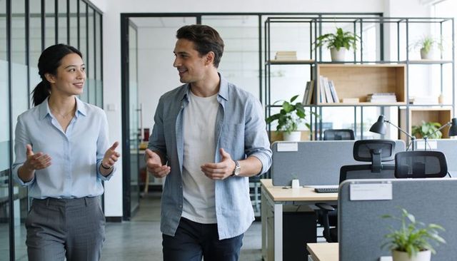 Walking coworkers discussing ideas in modern open-plan office with plants and workstations