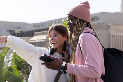Smiling diverse students pointing and navigating campus with smartphone and notebook
