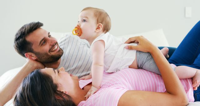 Young family enjoying bonding moments with their baby on bed. Perfect for parenting blogs, family-oriented advertisements, childcare services promotion, and articles about family life and bonding.