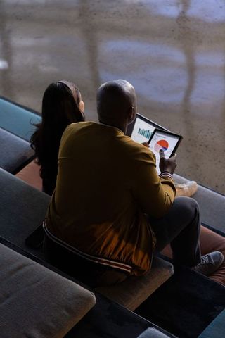 Diverse coworkers reviewing analytics on tablet while sitting on tiered lounge bench