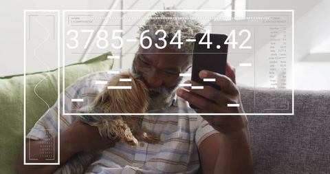 Senior man cuddling small dog while checking smartphone on sunlit sofa with hud overlay