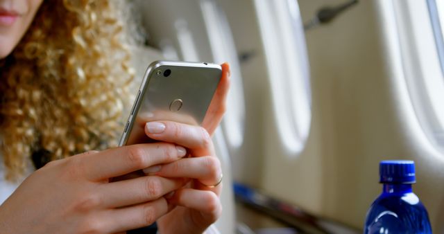 This scene shows a woman using her smartphone while traveling on an airplane. Ideal for topics related to air travel, modern technology, communication, and in-flight convenience. Suitable for travel blogs, airline advertisements, and tech-related articles.