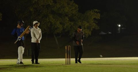 Night cricket bowler delivering fast ball under floodlights while batsman misses shot