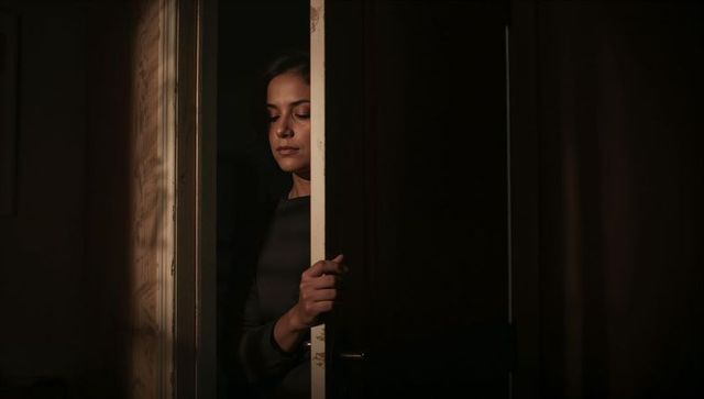 Woman standing in doorway holding door seam in moody low-key chiaroscuro interior portrait