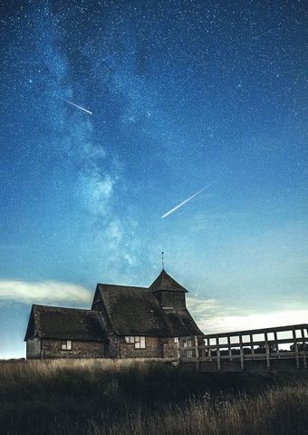Historic timber boathouse under milky way with meteor streaks and star-filled night sky