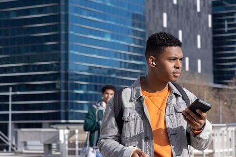 Urban African American Teen Walking, Checking Smartphone on City Bridge with Backpack