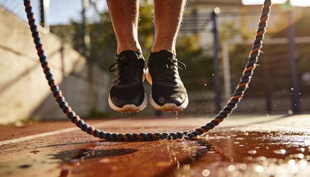 Adult jumping rope on wet outdoor court backlit splashing water with black running shoes