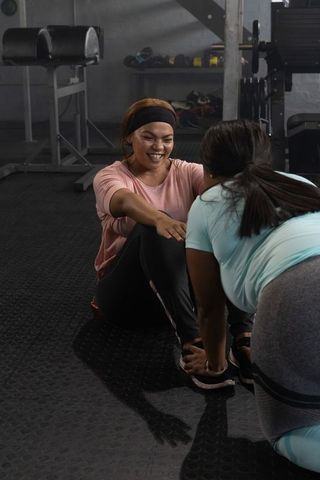 African american women stretching and laughing during partner workout in gym with weights