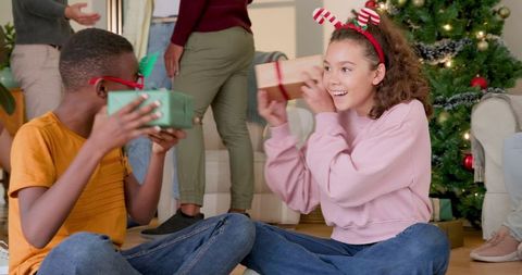 Cheerful kids exchanging gifts by christmas tree