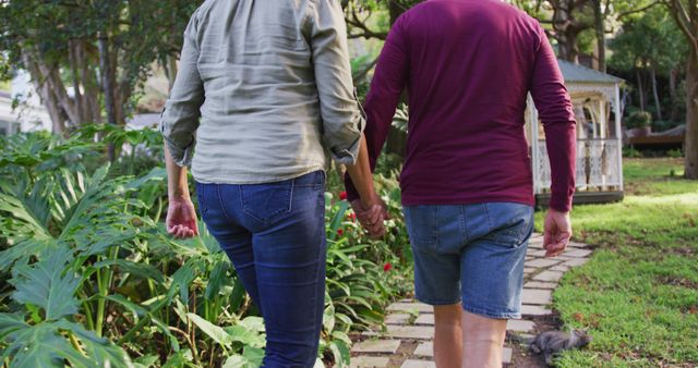 Rear view of happy senior caucasian couple holding hands, walking in garden. happy, healthy retirement lifestyle at home.
