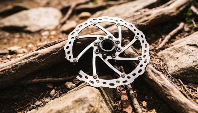 Mountain bike disc rotor lying on forest floor among roots rocks gravel metal hub detail