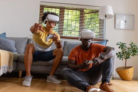 Diverse friends playing VR games in bright living room with white headsets and controllers