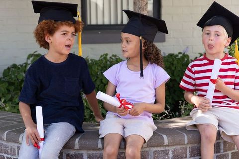 Young students celebrating kindergarten graduation wearing mortarboards and holding diplomas