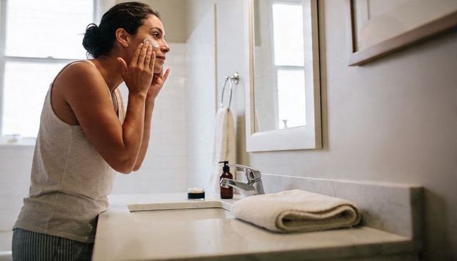 Woman applying facial cream at bathroom sink morning skincare routine mirror minimalist