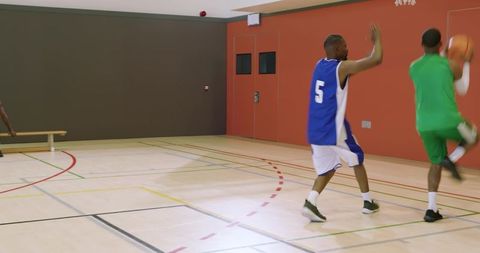 African american men playing indoor basketball, defender contesting layup and rebound