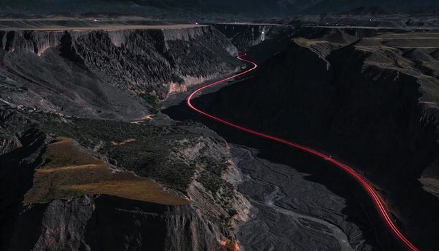 Aerial canyon highway glowing with red light trail winding through dramatic night ravine