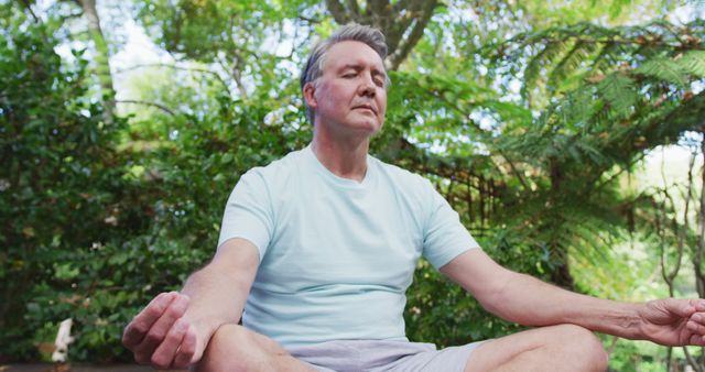 Relaxed senior caucasian man practicing yoga sitting in lotus position meditating in garden. healthy retirement lifestyle.