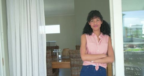 Confident african american woman leaning in sunlit doorway wearing pink top and jeans
