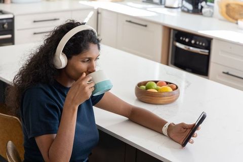African american woman sipping coffee and checking phone at modern kitchen island