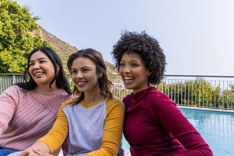 Multicultural friends laughing poolside during sunlit backyard gathering, casual lifestyle