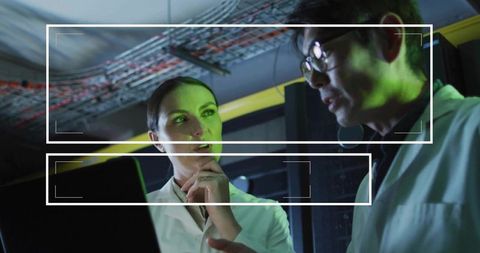 Two engineers collaborating in neon-lit data center examining laptop and network cables