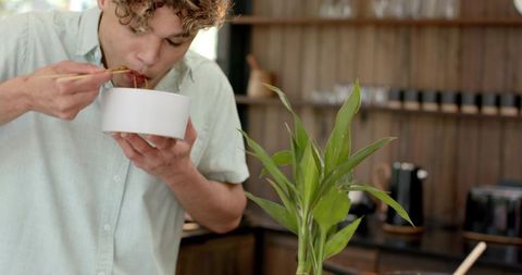 Young Man Eating Noodles with Chopsticks in Modern Kitchen
