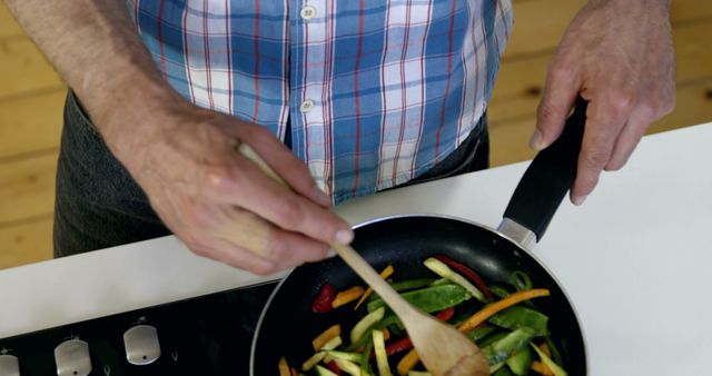 Shows a man cooking mixed vegetables in a frying pan. Useful for topics on healthy eating, meal preparation, home cooking, and kitchen activities.