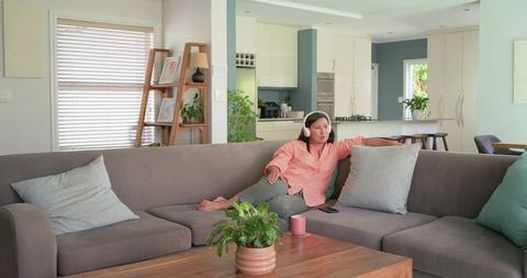 Asian woman reclining on gray sectional wearing headset and relaxing in pastel living room