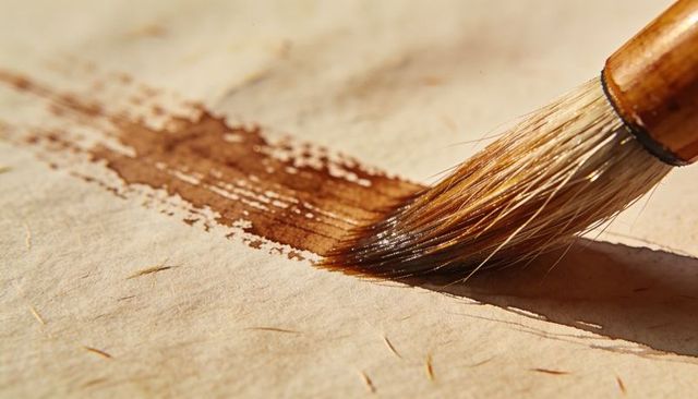 Applying brown watercolor wash with natural-hair brush on textured handmade paper macro