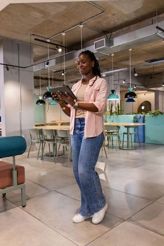 African american woman using tablet in modern coworking space with teal accents and plants