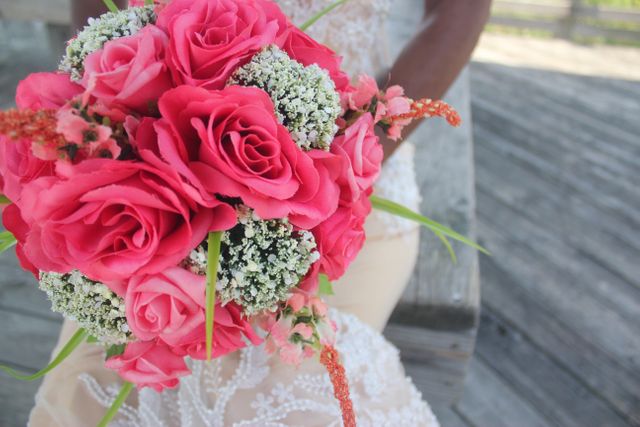 Close-up of a bride holding a vibrant bouquet of pink roses and white flowers. Ideal for wedding blogs, florist advertising, and marriage ceremony promotions.