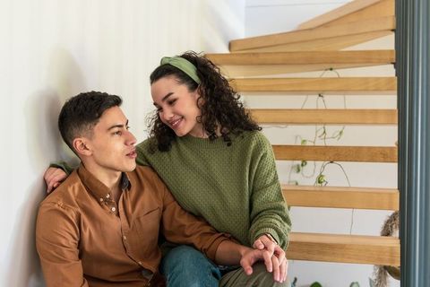 Young couple sharing tender moment on wooden stairs, holding hands and smiling in cozy home light