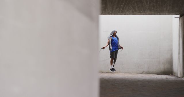 Young man jumping rope in urban concrete environment wearing athletic gear. Suitable for content related to fitness, health, urban lifestyles, outdoor workouts, and athletic training. Great for promoting sports equipment, exercise routines, and balanced lifestyles.
