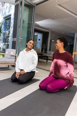 Multicultural women kneeling on yoga mats practicing gentle yoga beside open folding doors