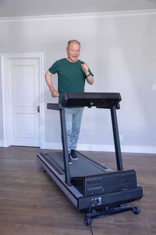 Senior asian man walking on treadmill at home for senior cardio fitness and wellness