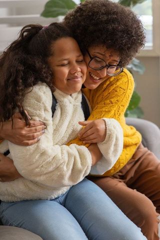 Parent hugging child on sofa after school embracing warm cozy family moment home