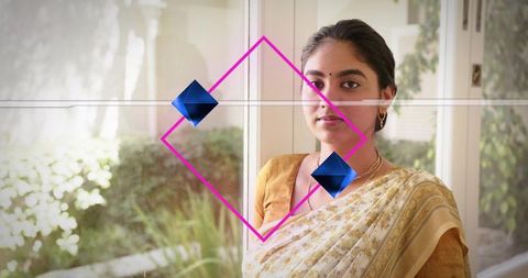 Young indian woman standing by window wearing cream saree with magenta diamond graphic overlay