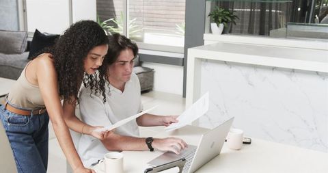 Diverse Couple Analyzing Paperwork At Home With Laptop Coffee