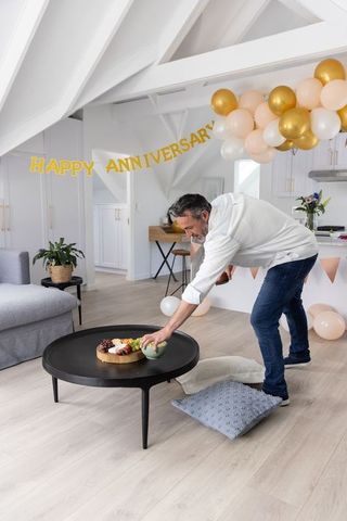 Middle-aged man arranging anniversary decorations in bright modern living room