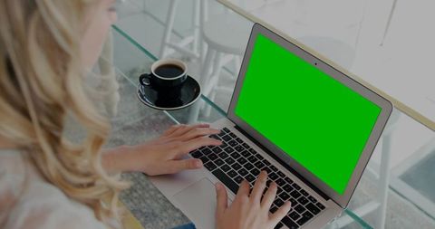Freelancer typing on laptop with green screen at glass table cafe with coffee cup modern workspace
