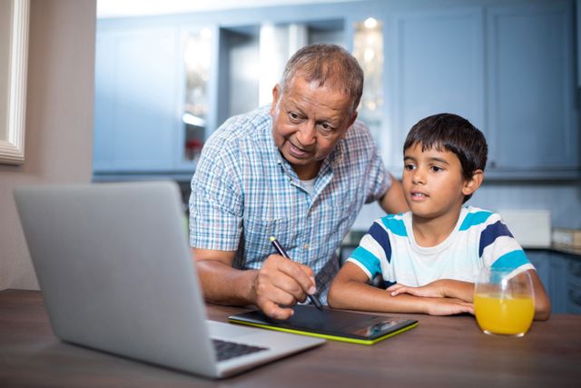 Man writing on tablet while using laptop with grandson at table at home