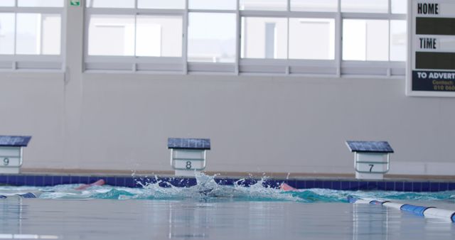This image shows an empty indoor swimming pool with clear water and visible lanes. The scoreboard in the background hints at a sports facility or school environment, making it ideal for health, fitness, and sports-related materials. It can be used to signify preparation for a swimming competition, promoting aquatic centers, or illustrating athletic training concepts.